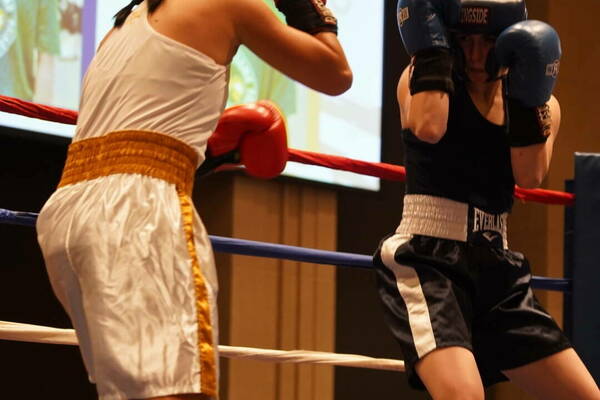 Two women boxing, one wearing a white top and shorts, the other a black top and shorts